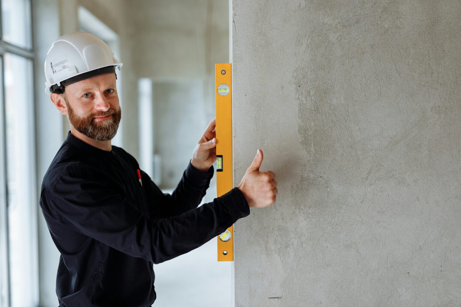 Contractor wearing a hard hat using a level tool on a wall, emphasizing safety and the importance of liability insurance for contractors