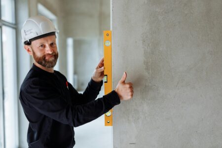 Contractor wearing a hard hat using a level tool on a wall, emphasizing safety and the importance of liability insurance for contractors